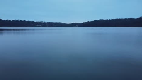 Drone-flying-just-above-lake-water-and-ducks-after-sunset-with-blue-colors-and-overcast-skies-during-winter