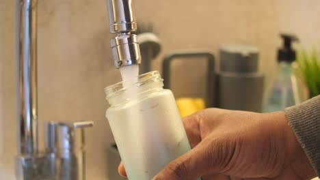 a close-up shot of a hand pouring water from a kitchen faucet into a glass jar