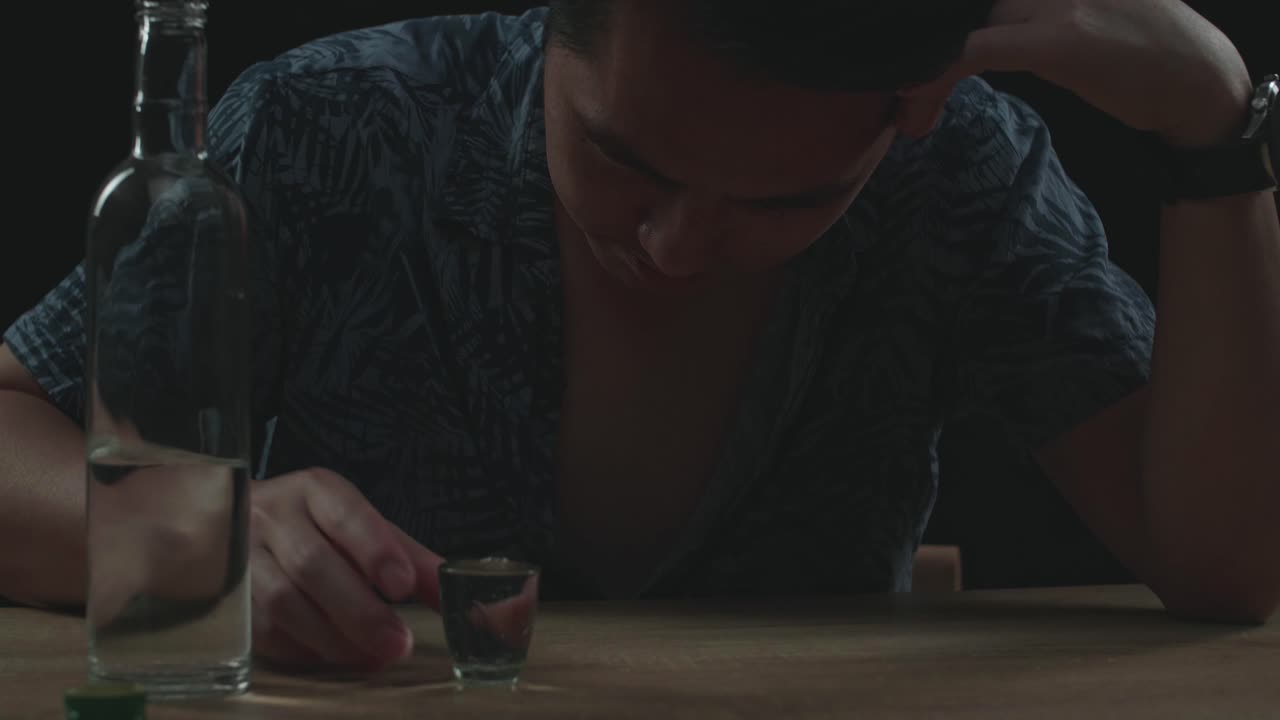 술에 취한, 우울한 아시아 남자가 검은 바탕에서 술을 마시기 전에 글라스에 보드카를 부어