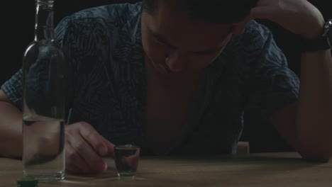 un hombre asiático borracho y deprimido vertiendo vodka en un vaso antes de beber en un fondo negro.