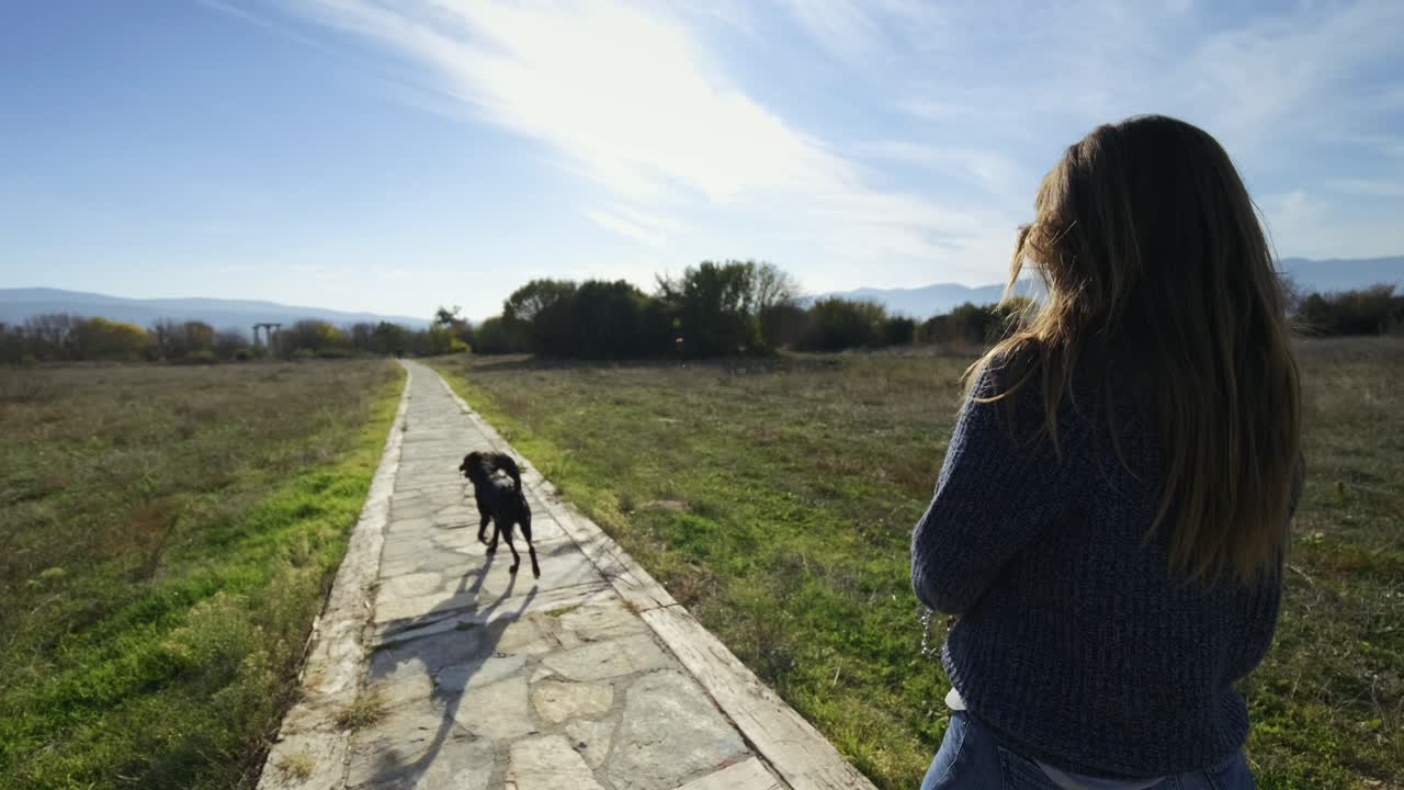 la mujer camina en la naturaleza con su perro negro, la cámara los toma por detrás