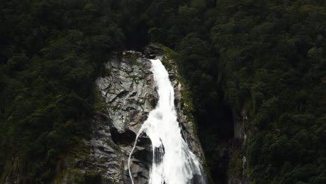 powerful waters of lady bowens waterfall flow down the slope bearween deep green forest in milford sound, southland, south island, new zealand, fjordland national park