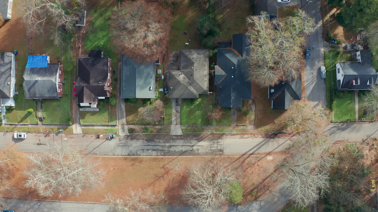 A slow overhead panning down a row of scenic and historic single family homes, with yards in the front and back, under the shade of the beautiful fall tree canopy in Atlanta, Georgia.