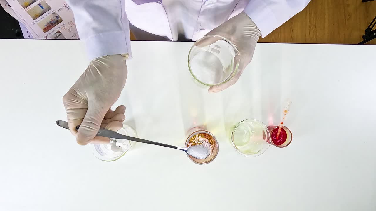 Scientist conducts a colorful liquid experiment on a white table using beakers and spoons under bright lighting
