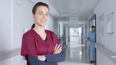 Portrait-of-caucasian-female-doctor-wearing-scrubs,-smiling-in-corridor,-slow-motion