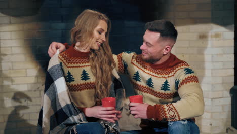loving couple is warming in the evening near fireplace. same knitted sweaters on male and female. love story concept.