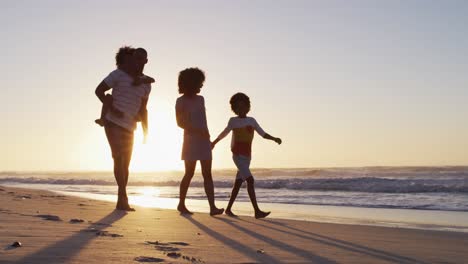 Familia-Afroamericana-Divirtiéndose-Caminando-Juntos-Durante-El-Atardecer-En-La-Playa