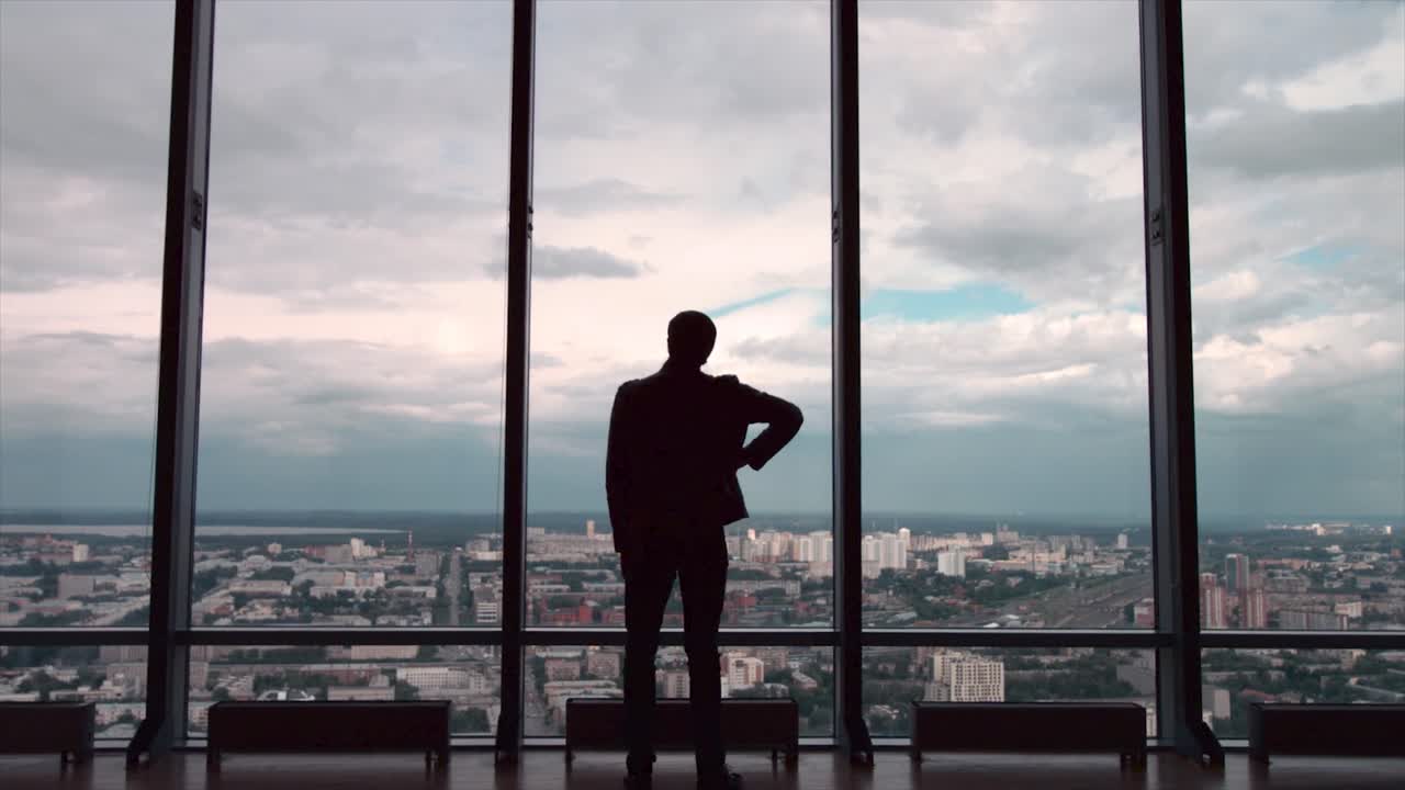 un hombre de negocios contemplando la vista de la ciudad desde una ventana de gran altura.