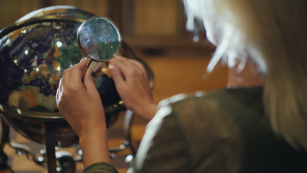 손에 돋보기를 가진 여자는 큰 지구 다시 보기를 검사합니다.