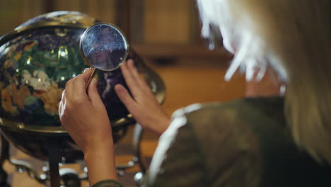 woman with magnifying glass in hand examines big globe back view