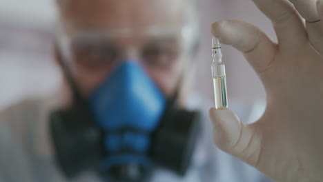 extreme close-up of a scientist in a blue respirator and protective glasses the developer of the coronavirus vaccine is holding a white transparent ampoule. the doctor looks at the new vaccine. high quality 4k footage