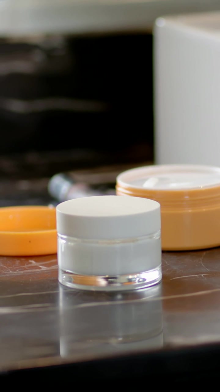 Video verticale: Vaso bianco centrato su una toeletta, la telecamera si sposta per mostrare crema arancione e un tubetto.