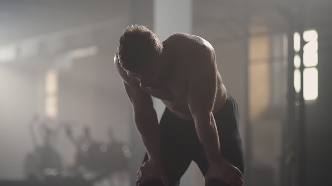 체육관에서 집중적인 운동을 한 후 휴식을 취하는 지친 젊은 남성. 체육관에서 근력 훈련 운동을 한 후 피곤한 건강한 남성. 강렬한 운동을 한 후 서서 휴식을 취하는 피곤한 남성 피트 모델.