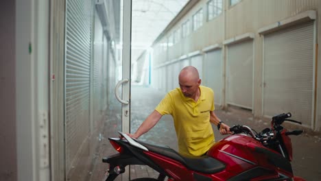 Side-view.-A-bald-man-driving-instructor-in-a-yellow-T-shirt-drives-a-red-moped-into-the-garage.-End-of-the-working-day-at-the-motorcycle-school