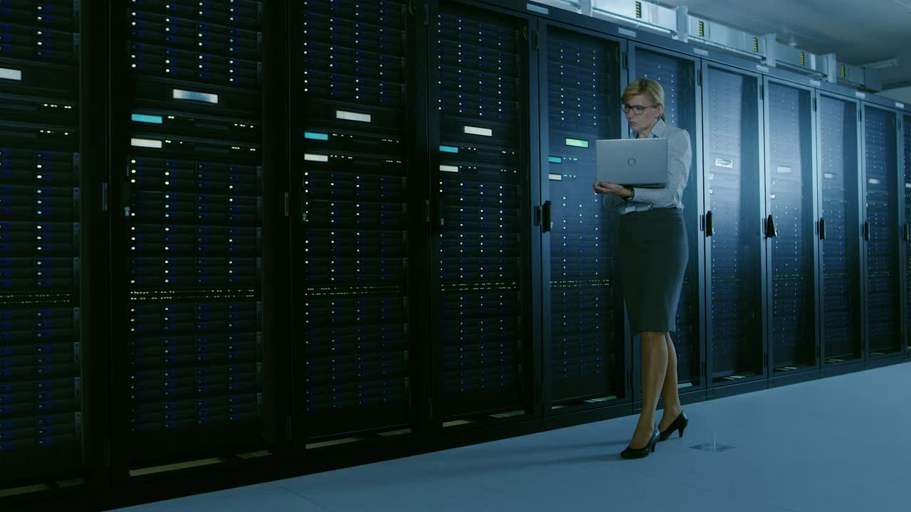 en el centro de datos la mujer especialista en ti camina a lo largo de la fila de bastidores de servidores operativos, comprobando el funcionamiento normal. moderno centro de datos operativos de telecomunicaciones de alta tecnología.