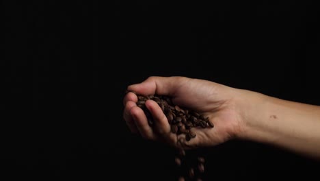 hand holding roasted coffee beans on black background, slow motion