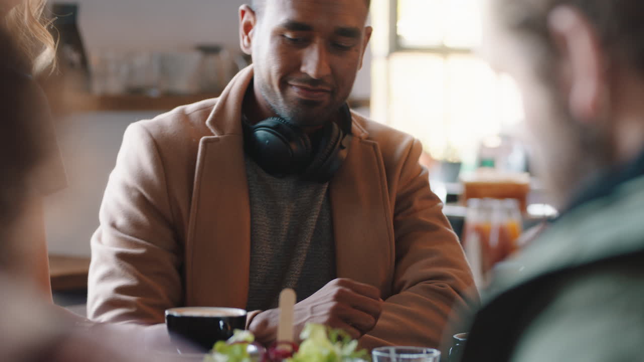 joven hombre de negocios usando un teléfono inteligente en una cafetería navegando mensajes disfrutando del servicio con la camarera sirviendo café