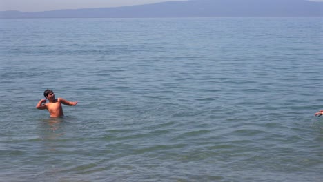 slow motion 100fps footage of two caucasian brothers , playing with a small beach ball at sea of kalamata, right pan medium shot