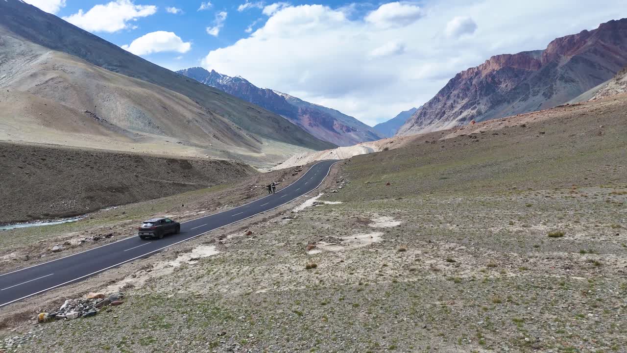 Aerial drone shot focusing on a vehicle traveling the straight route amid Ladakh’s stark, rugged environment.