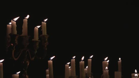 a group of white candles some on a candelabra lit up and running for a while