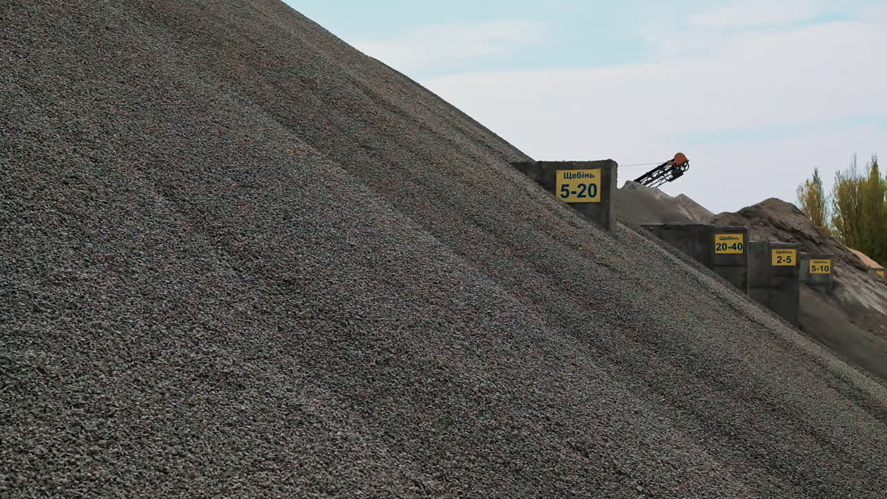 Large pile of gravel. Building materials in the concrete plant outdoors. Gravel production. Crushed stones on a big heap against the clear sky.