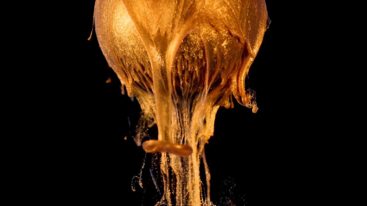 Goldglänzende Farbe fließt langsam aus der Kugel.