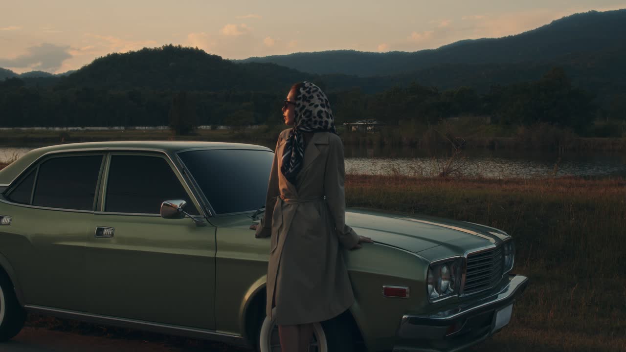 Woman in Vintage Trench Coat by Retro Car at Sunset