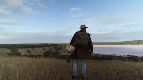 australian swag man in historical gear looks at a salt lake in the outback