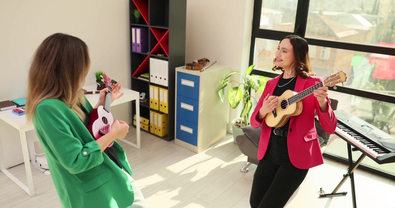 Aydınlık ofiste müzik çalmakla meşgul kadınlar ukulele tutuyor