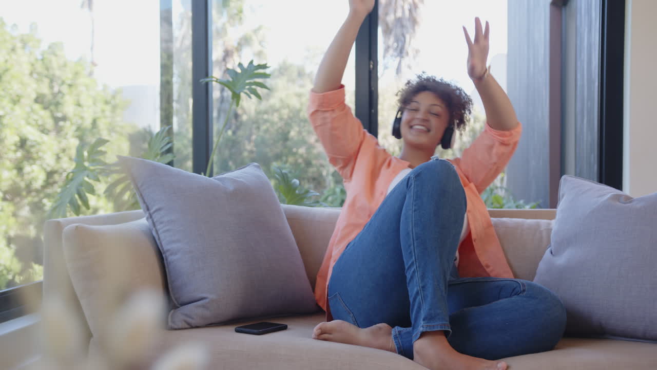 Listening to music with headphones, woman relaxing on couch with smartphone nearby