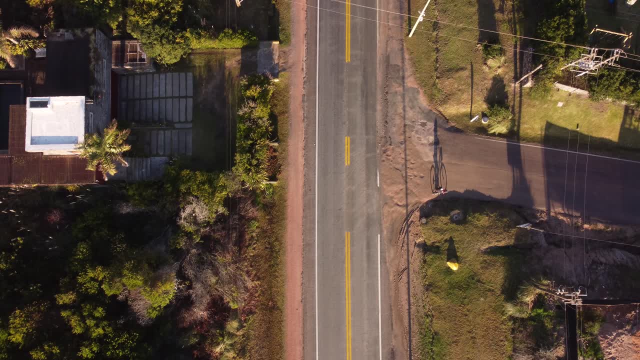 Inquadratura aerea dall'alto di una persona in bicicletta che cammina lungo la strada al tramonto.
