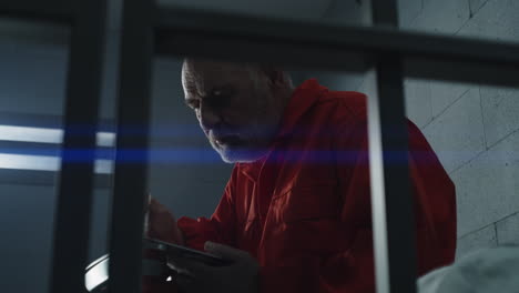 Close-Up-of-Prisoner-in-Orange-Uniform-Holding-Metal-Bars-in-Prison-Cell----------(Stock-Footage)