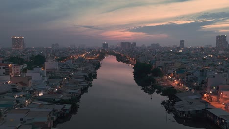 Evening-view-along-canal-in-Ho-Chi-Minh-City,-Vietnam-with-shanty-houses-illuminated-and-reflection-part-two