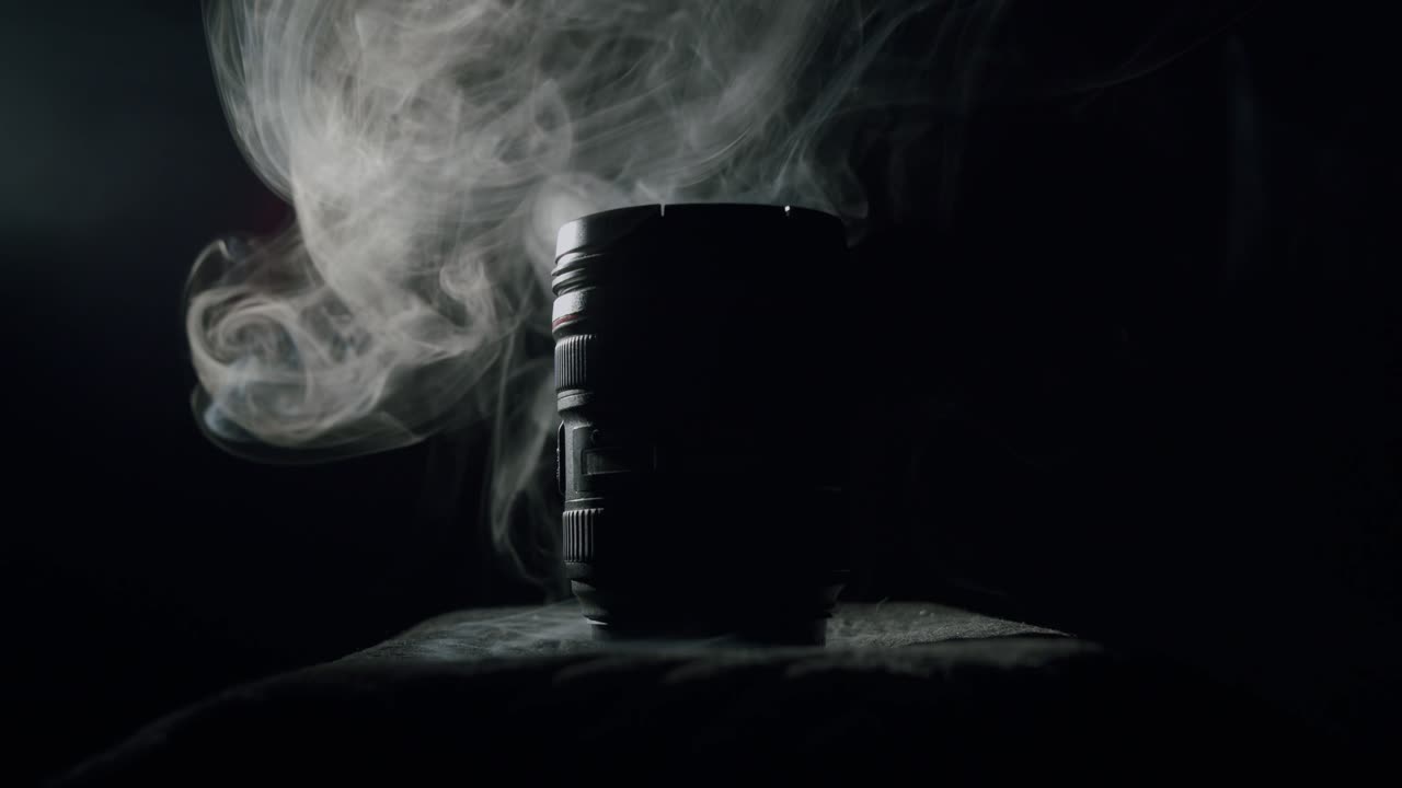 White smoke behind a modern photography lens in a dark room in a silhouette lighting