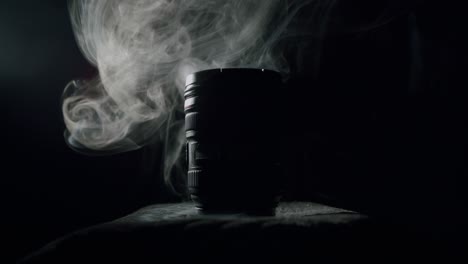 white smoke behind a modern photography lens in a dark room in a silhouette lighting