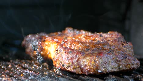 a pair of meat tongs turn a nearly cooked juicy rib eye steak on a grill