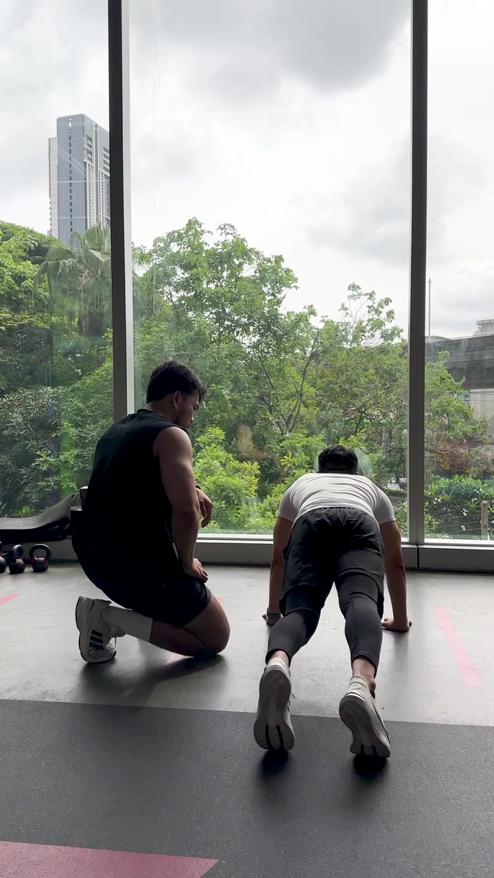 Trainer instructs client on floor exercise in modern gym with large windows and natural daylight