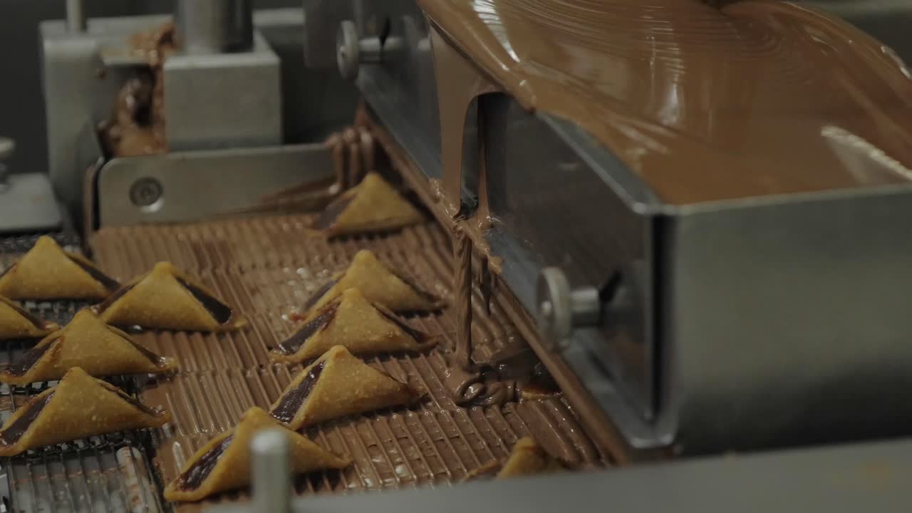 Close-up of melted chocolate pouring over triangular pralines on a factory conveyor belt