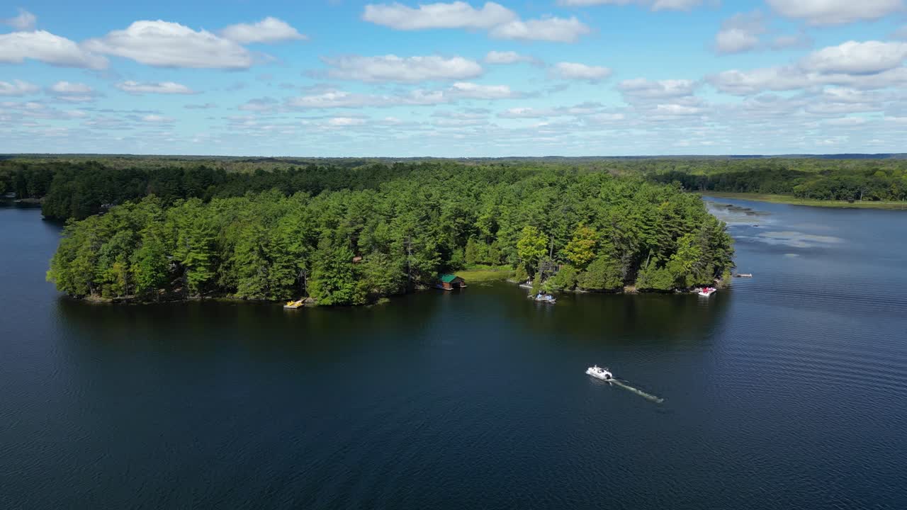 Drone reveals island and open lake as a boat passes leaving soft wake trails behind approaching private docks