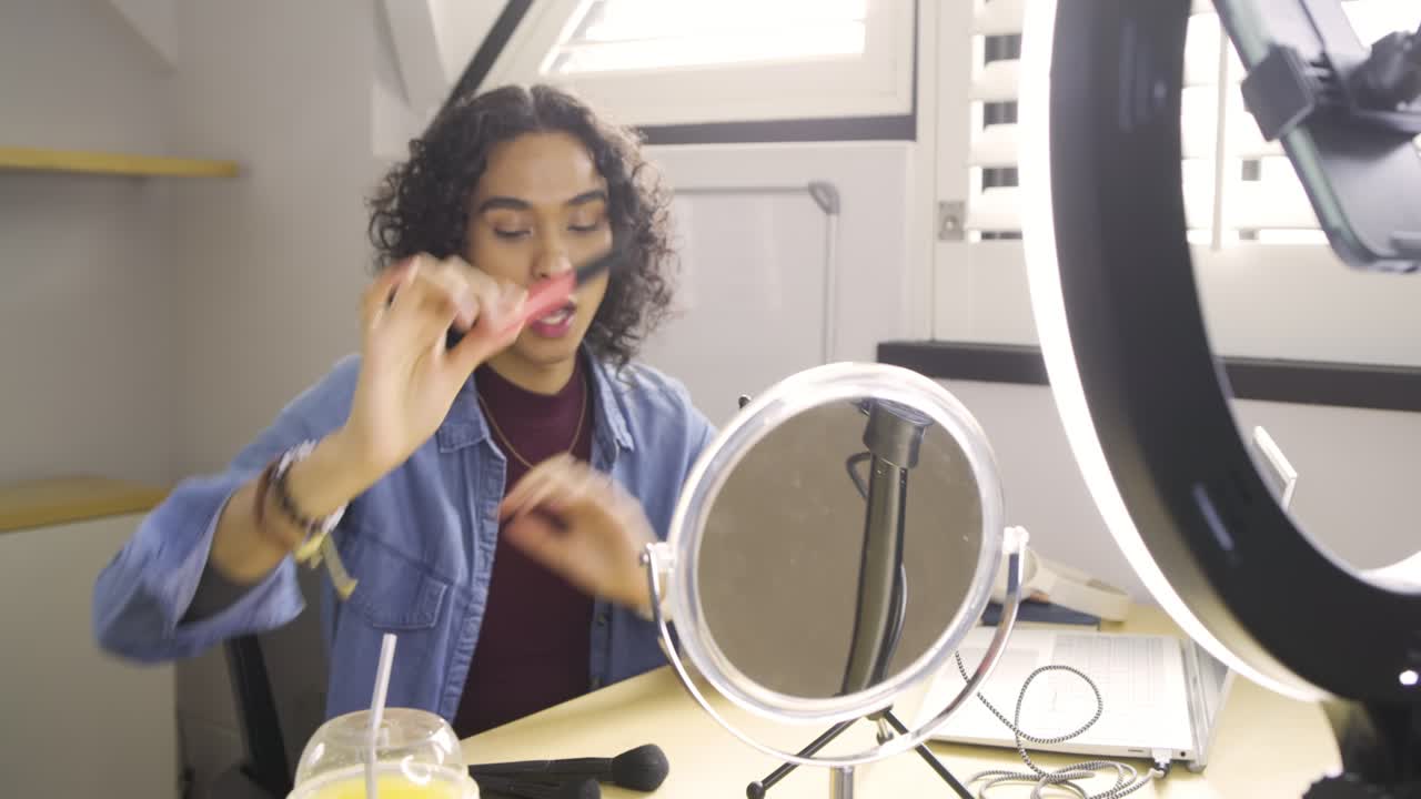Starting tutorial non-binary creator greeting camera at studio showcasing lip gloss, filling brows