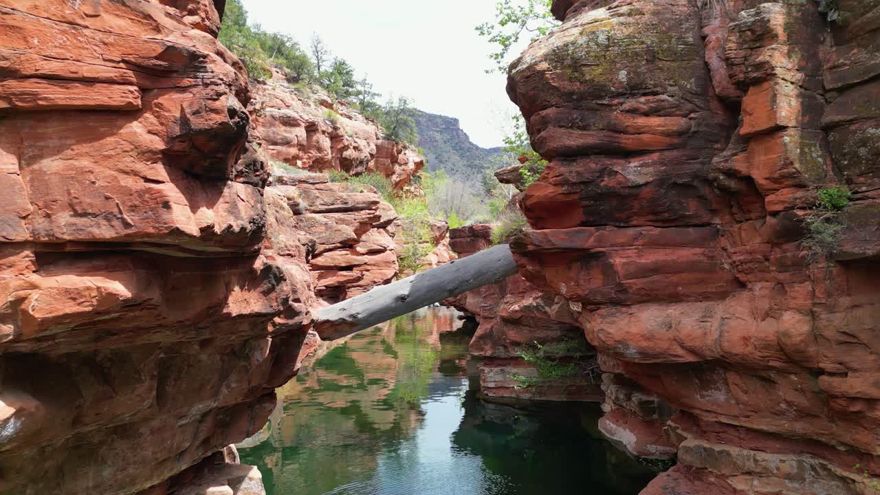 Arizona'daki sakin dere suyu ve doğal kaya oluşumlarıyla kırmızı kaya kanyonunda uçan drone çekimi. Manzaralı çöl manzarası ve açık hava macera doğa çekimi.