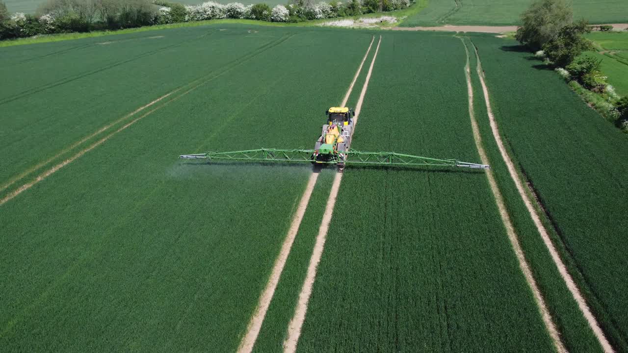 un dron disparó siguiendo y descendiendo hacia un tractor amarillo y verde, rociando campos de trigo con su maquinaria detrás