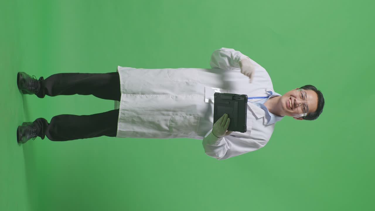 Full Body Of Asian Man Scientist Smiling And Pointing To A Tablet While Standing On The Green Screen Background In The Laboratory
