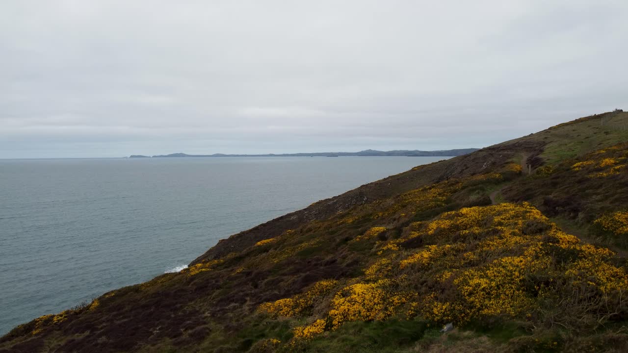 antena de drones ascendente con camino costero mar tranquilo con pembrokeshire en la distancia reino unido 4k