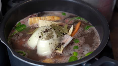 ゆっくりと沸騰し,野菜と骨のスープをナイフで混ぜる