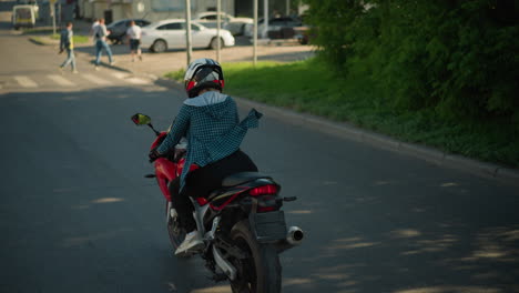 un jinete en una bicicleta eléctrica roja cruzando a lo largo de una carretera urbana serena, el jinete está usando una camisa a cuadros y un casco, dirigiéndose hacia un cruce de peatones con peatones en la distancia