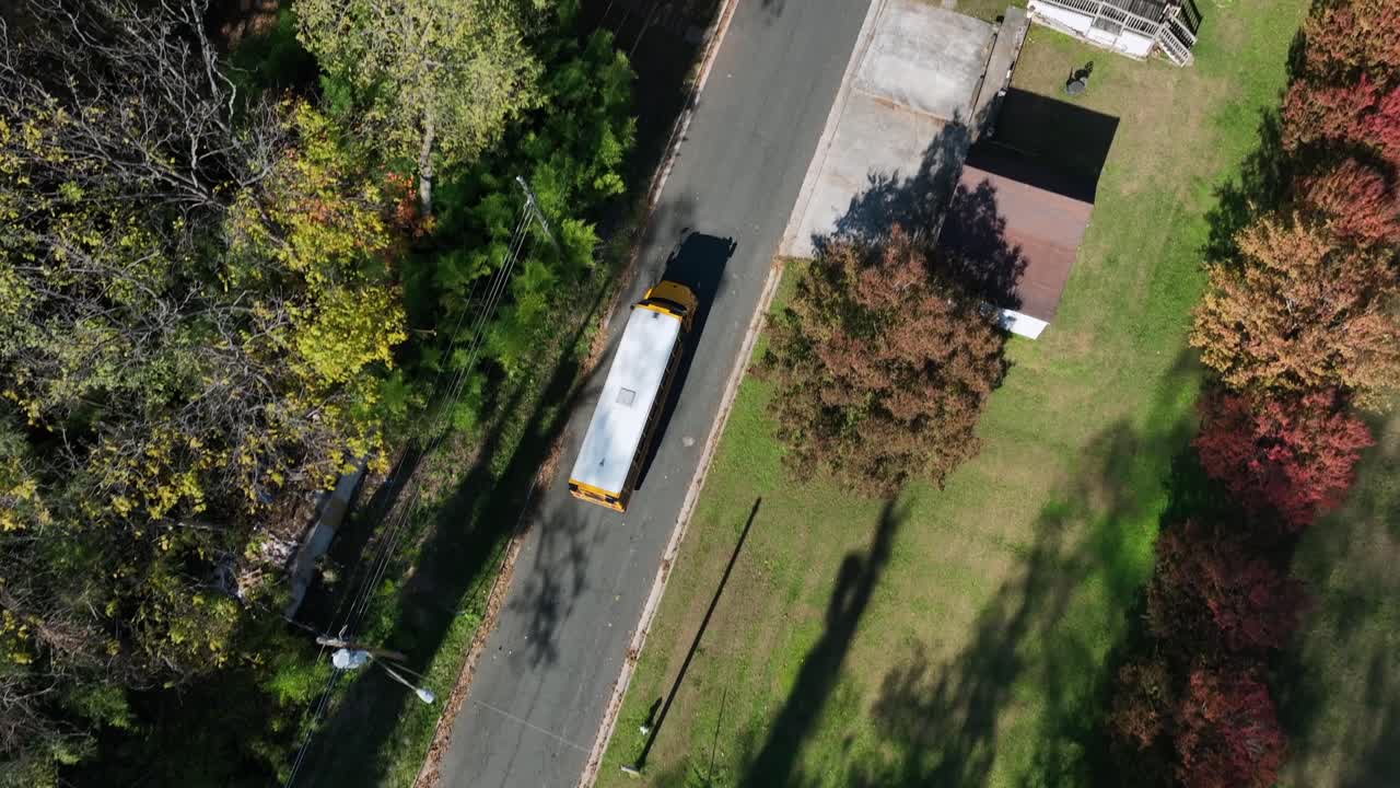 Yellow school bus on street of American neighborhood. Aerial tilt up wide shot. Sunny day in fall season. Quiet suburb in USA. Public transport for kids in America