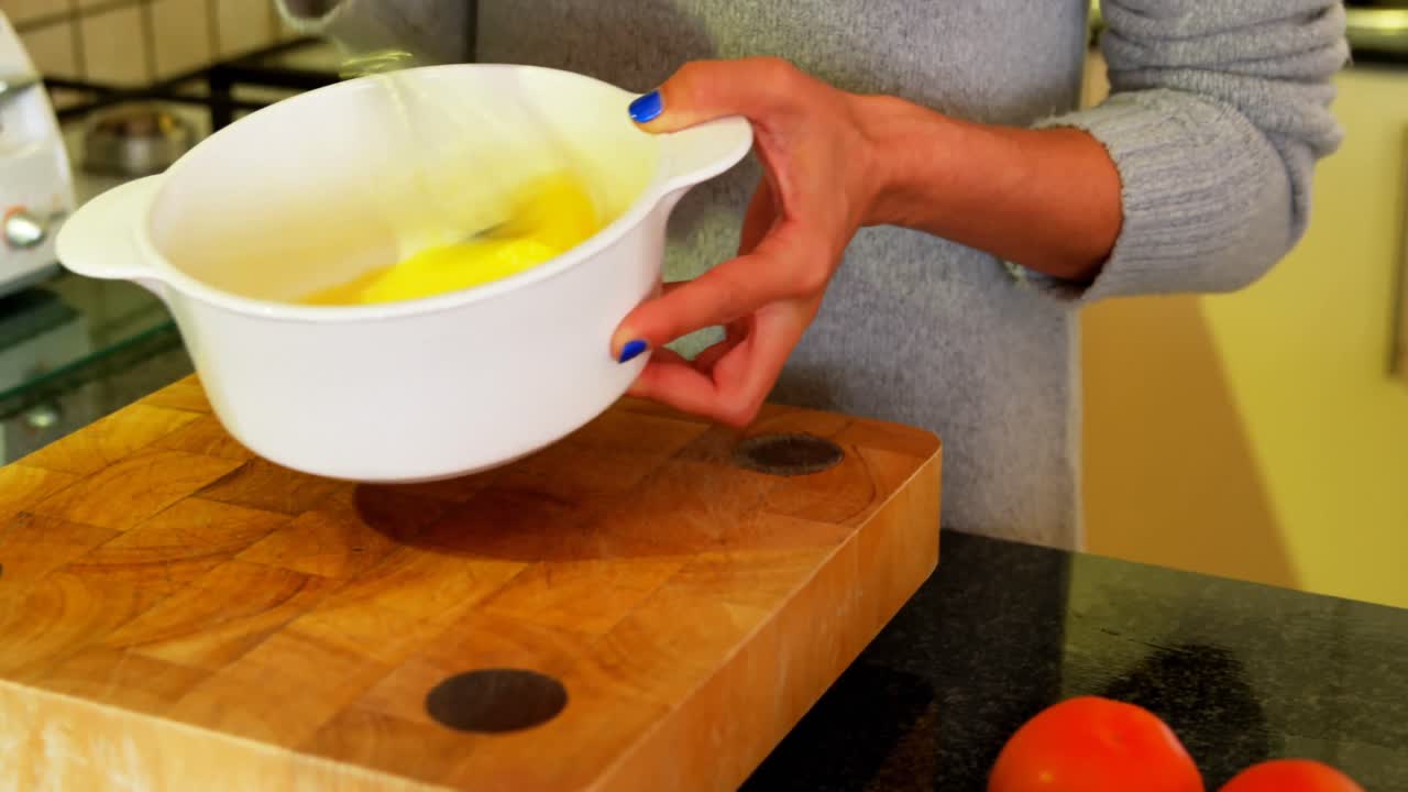 mujer removiendo yema de huevo en el cuenco en la cocina en casa 4k