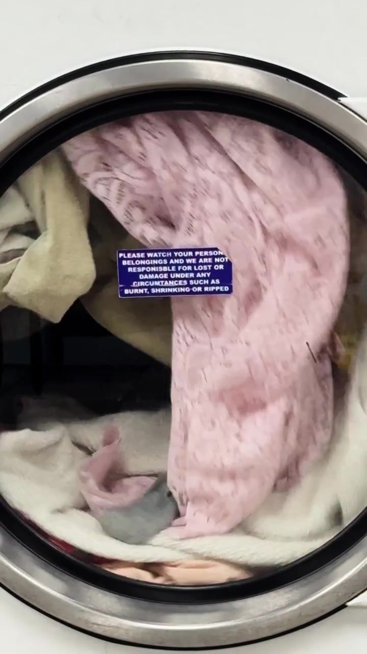 Colorful laundry spinning in front-loading washing machine at laundromat interior