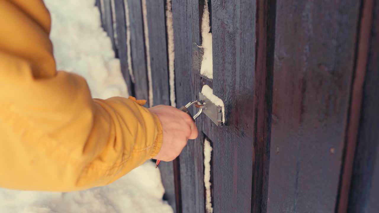Man ontgrendelt bevroren hangslot van houten poort in de winter